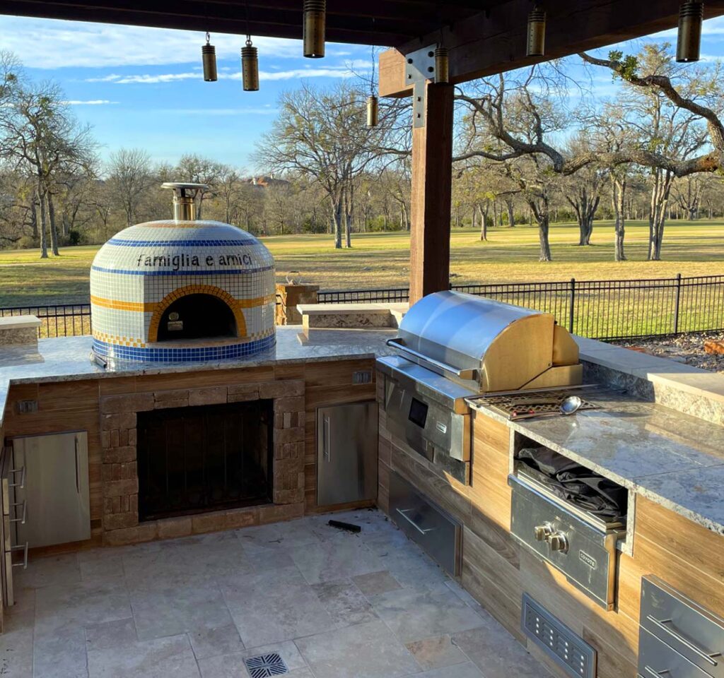 Custom outdoor kitchen with pizza oven, refrigerated drawers, and stainless steel counters.