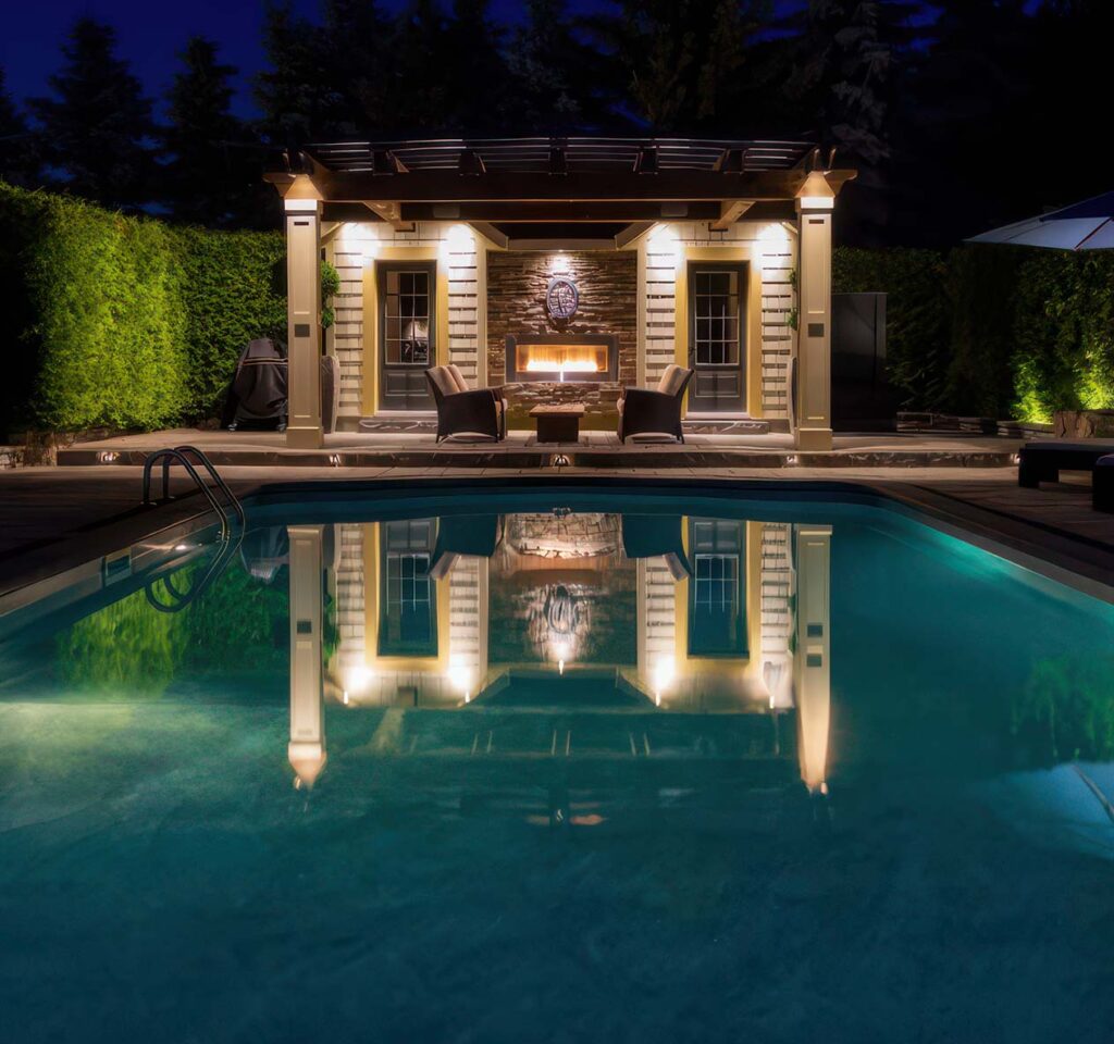 Pergola and outdoor seating area with beautiful lighting beside a pool.